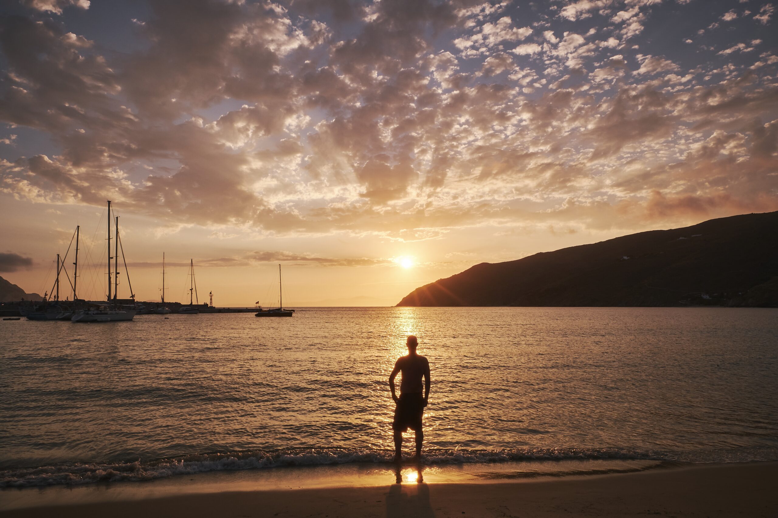 Jeune homme debout face à la mer au coucher du soleil — symbole de renaissance et de transformation intérieure en expatriation